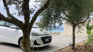 Ein weißes Auto vor einer Steinmauer mit Blick auf das Meer.