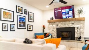 Een woonkamer met een open haard, foto's in lijsten aan de muur en een flatscreen televisie waarop streamingdiensten worden afgespeeld.