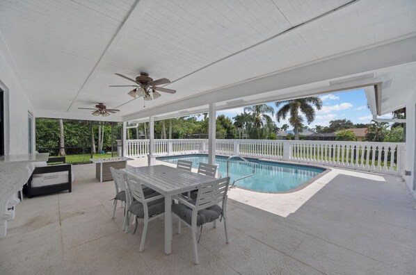 A covered outdoor area with a pool, white furniture, and a ceiling fan.