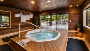 Un área de spa con un jacuzzi, suelo de madera y vistas al área de la piscina exterior.