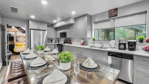 Una cocina moderna con electrodomésticos de acero inoxidable, un comedor con una mesa de vidrio para seis personas y vistas al exterior a través de un amplio ventanal.
