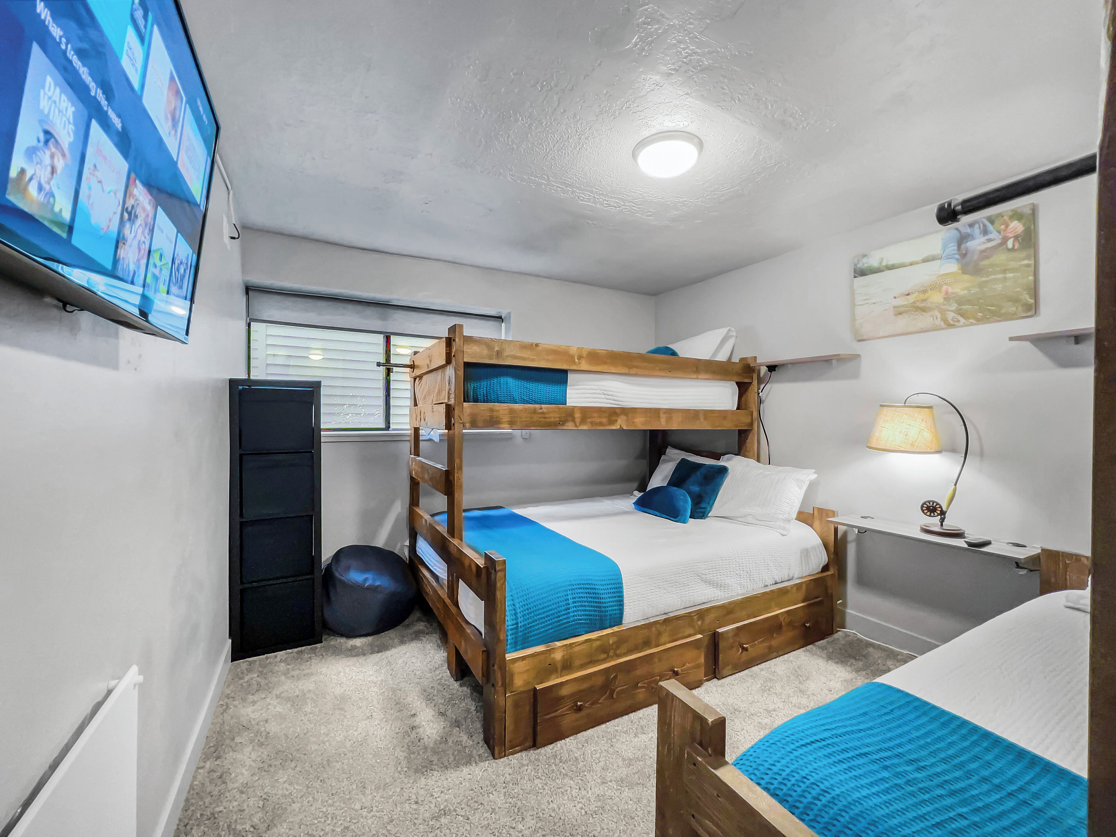 A bunk bed room with a television, a desk with a lamp, and a window with blinds.