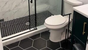 A modern bathroom with a glass-enclosed shower, a white toilet, and a hexagonal tile floor. - City Arts Apartment (Philadelphia)