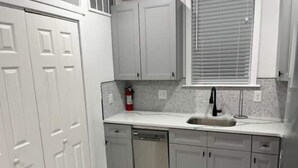 A kitchen with white cabinets, a stainless steel sink, and a tiled backsplash. - City Arts Apartment (Philadelphia)