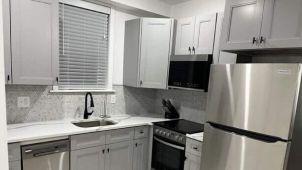 A modern kitchen with stainless steel appliances, white cabinetry, and a tiled backsplash. - City Arts Apartment (Philadelphia)