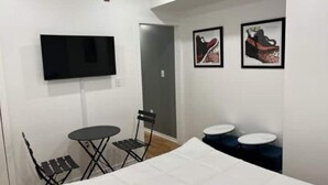 A hotel room with a bed, a TV mounted on the wall, a small table with chairs, and two round tables with stools. - City Arts Apartment (Philadelphia)