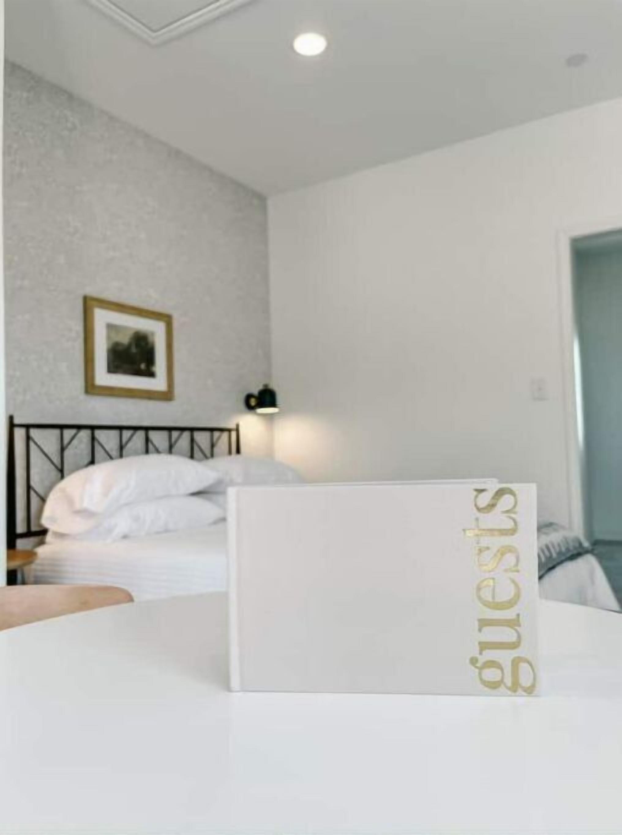 A hotel room with a neatly made bed, a framed picture on the wall, and a sign with the word 'guests' on the bed.
