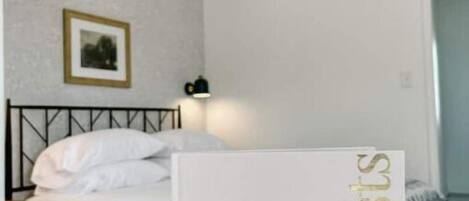 A hotel room with a neatly made bed, a framed picture on the wall, and a sign with the word 'guests' on the bed.