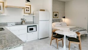 A compact kitchenette with a microwave, a refrigerator, and a sink. There is a small dining table with two chairs. The room has a bed with a white comforter and a headboard. - Upscale studio with skyline view (Abilene)