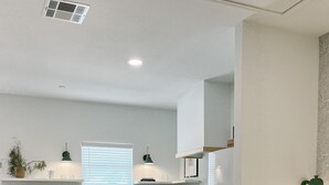 A modern hotel room with a bed, a dining area with chairs, a kitchen with a sink and stove, and a window with blinds.