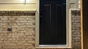 A black door with a window above it, a light fixture above the door, and a stone wall to the left.