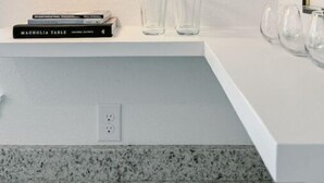 A modern kitchen with a white countertop, a green pendant light, and a white shelf with books and glasses.