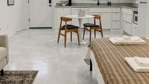 A compact, modern room with a kitchenette, a dining area with two chairs, a bed with a striped blanket, and a small rug.