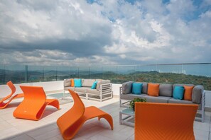 Eine Dachterrasse mit moderner orangefarbener und grauer Möbel, einem Glasgeländer und einem schönen Panoramablick auf die Landschaft.