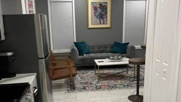 A compact kitchen with a refrigerator, stove, and cabinets. There is a grey sofa with a coffee table and a rug in the living area.