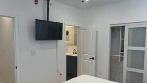 A bedroom with a bed, a TV mounted on the wall, a closet with sliding doors, and a bathroom visible through an open door.