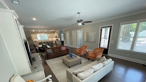 A spacious living room with a large white sofa, two armchairs, and a dining area with a chandelier.