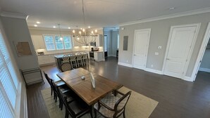 A spacious kitchen with modern appliances, a dining area with a wooden table and chairs, and a large chandelier.