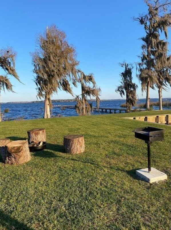 A grassy area with trees, a wooden bench, and a grill. - Waterfront Tiny Home (Crescent City)