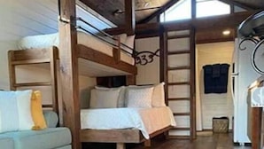 Interior rústico de cabana com beliches de madeira, um sofá e uma escada que dá para um mezanino.