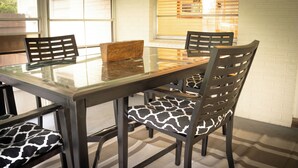 Un coin repas avec une table à plateau en verre, quatre chaises dotées de coussins à motifs et un mur en briques en arrière-plan.