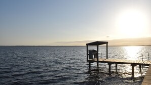 Une jetée en bois s’avançant dans une étendue d’eau calme, avec un petit abri à son extrémité.