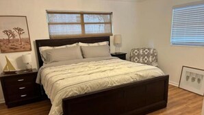 Une chambre à coucher avec un lit en bois, une table de chevet, une chaise et une fenêtre avec des stores.