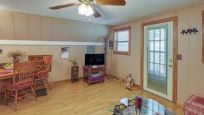 Un salon avec un plancher en bois, un ventilateur de plafond, un téléviseur, une table à manger avec des chaises et une porte avec une fenêtre.