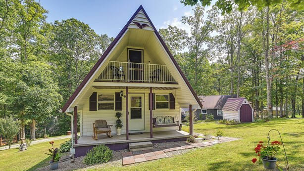 Une maison à deux étages avec un balcon, une véranda dotée d’un banc et un petit abri de jardin à l’arrière-plan.