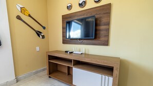 A room with a wooden console table, a flat-screen TV mounted on a wooden panel, and two paddleboards on the wall. - Caravelas (Marechal Deodoro)