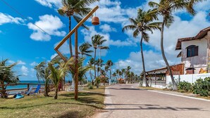 A coastal road lined with palm trees and a beachside area with lounge chairs. - Caravelas (Marechal Deodoro)