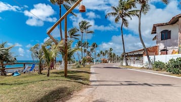 A coastal road lined with palm trees and a beachside area with lounge chairs.