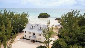 Une maison à deux étages dotée d’un porche abrité, entourée d’une végétation luxuriante et donnant sur une plage.