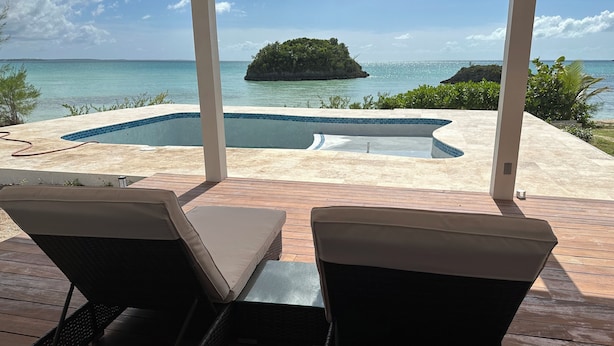 Un espace piscine comprenant deux chaises longues, une terrasse en bois et une vue sur l’océan et une île.