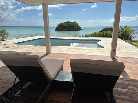 A pool area with two lounge chairs, a wooden deck, and a view of the ocean and an island.