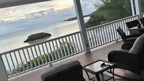 Un espace extérieur abrité avec des meubles en osier, une vue sur la mer et une petite île qui se profile à l’horizon.