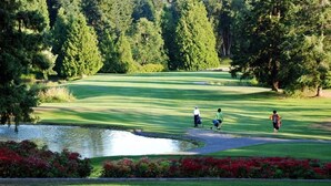 Un campo de golf con un estanque, rodeado de árboles y flores rojas.