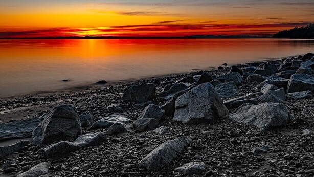 Una costa rocosa con un atardecer sobre una superficie de agua tranquila.