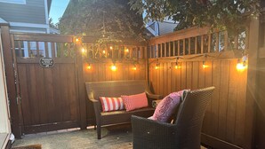 Un patio con mobiliario de mimbre, una cerca de madera y luces colgantes.
