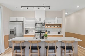 Eine moderne Küche mit weißen Schränken, einer zentralen Kochinsel mit Barhocker, Edelstahlgeräten und einem eingebauten Backofen.
