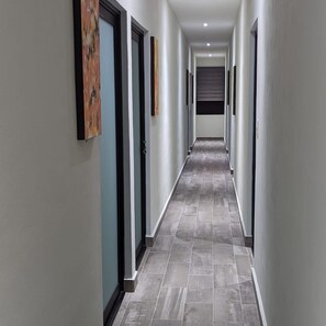 Un pasillo con puertas a ambos lados, piso de baldosas e iluminación empotrada en el techo.