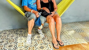Zwei Personen sitzen auf einem gemusterten Boden mit einer Hängematte, einem blauen Gemälde eines Wals und einer Kachelwand.