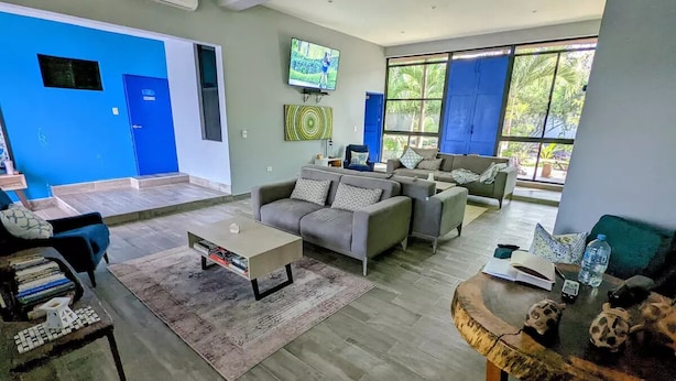 A spacious living room with a grey sofa, a coffee table, and a TV mounted on the wall. - The Blue Eco Lodge- double room 3 (Yalcón)