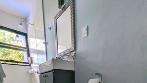 A bathroom with a toilet, a sink with a mirror, and a window. - The Blue Eco Lodge- double room 3 (Yalcón)