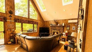 Una sala de estar acogedora con un sofá de cuero curvo, una chimenea, un televisor y paredes de madera.