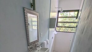 A bathroom with a toilet, sink, and mirror. There is a window with a view of trees.