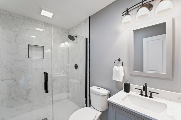 A modern bathroom with a glass-enclosed shower, a white toilet, and a sink with a mirror above it.