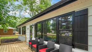 A covered deck with wicker furniture and red cushions, large windows, and a brick wall. - Sleek & Affordable 3 Bedroom/2 Bath in downtown Overland Park! (Overland Park)