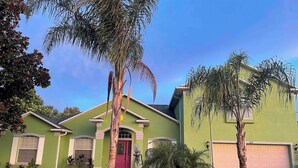 A green house with a red door, a garage, and palm trees in the yard. - Palm Coast Cozy apartment<br> (Palm Coast)