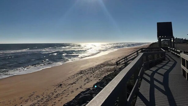A beach with a wooden boardwalk leading to a structure with a large screen. - Palm Coast Cozy apartment<br> (Palm Coast)